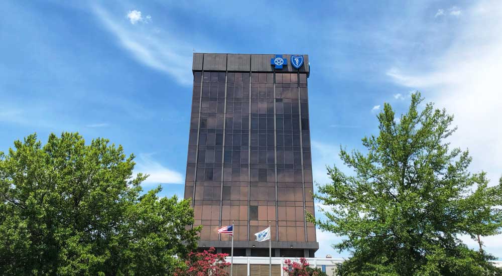 tall building with blue cross logo with trees and blue sky