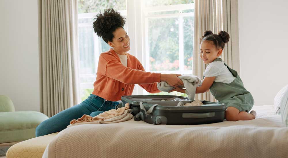 woman and child sitting on bed with suitcase open