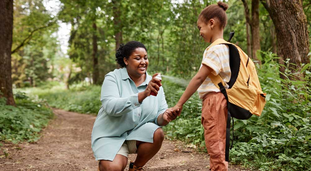 woman applying bug spray to child's arm in woods