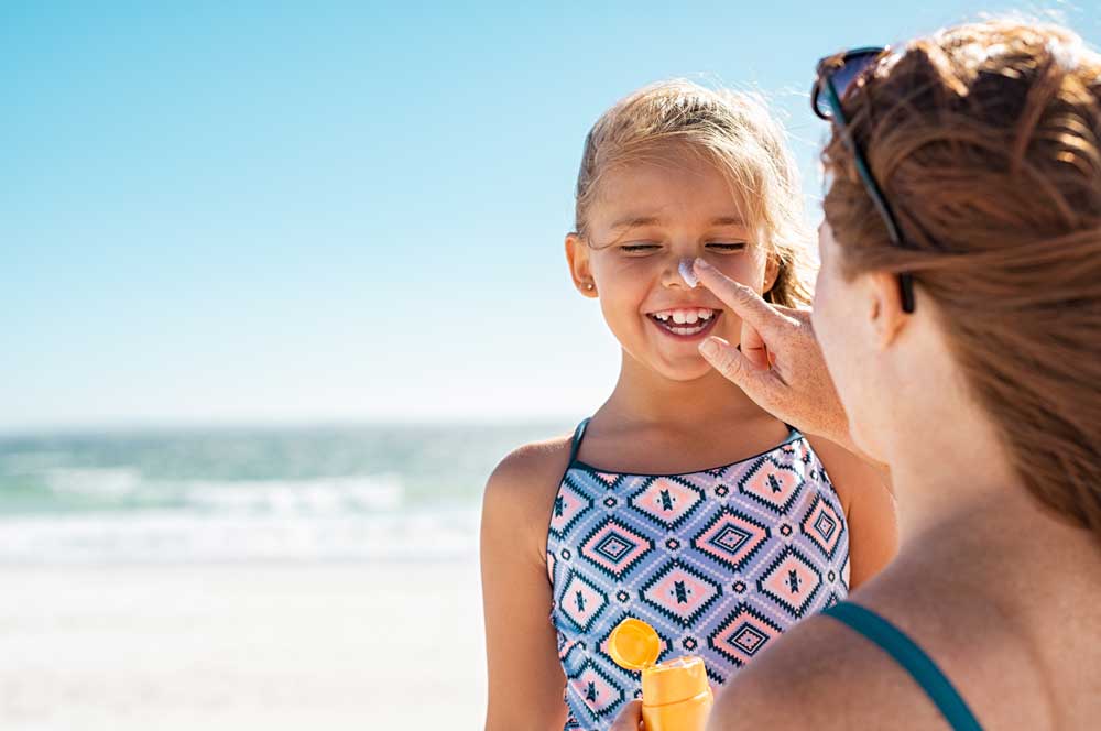 Little girl at beach with woman applying sunscreen to face